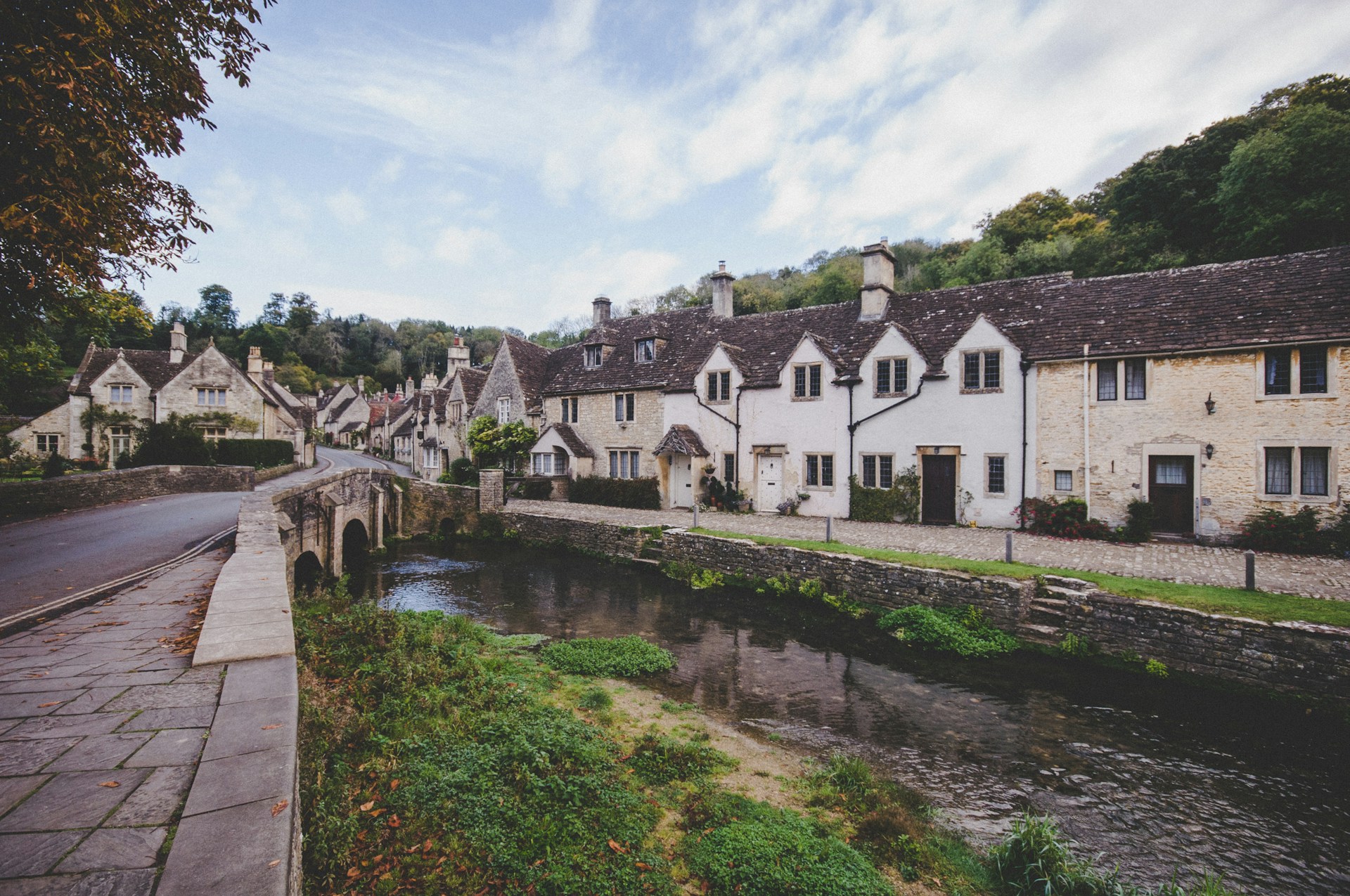 A row of honey-stone Cotswold cottages beside a stream and small bridge in an English village